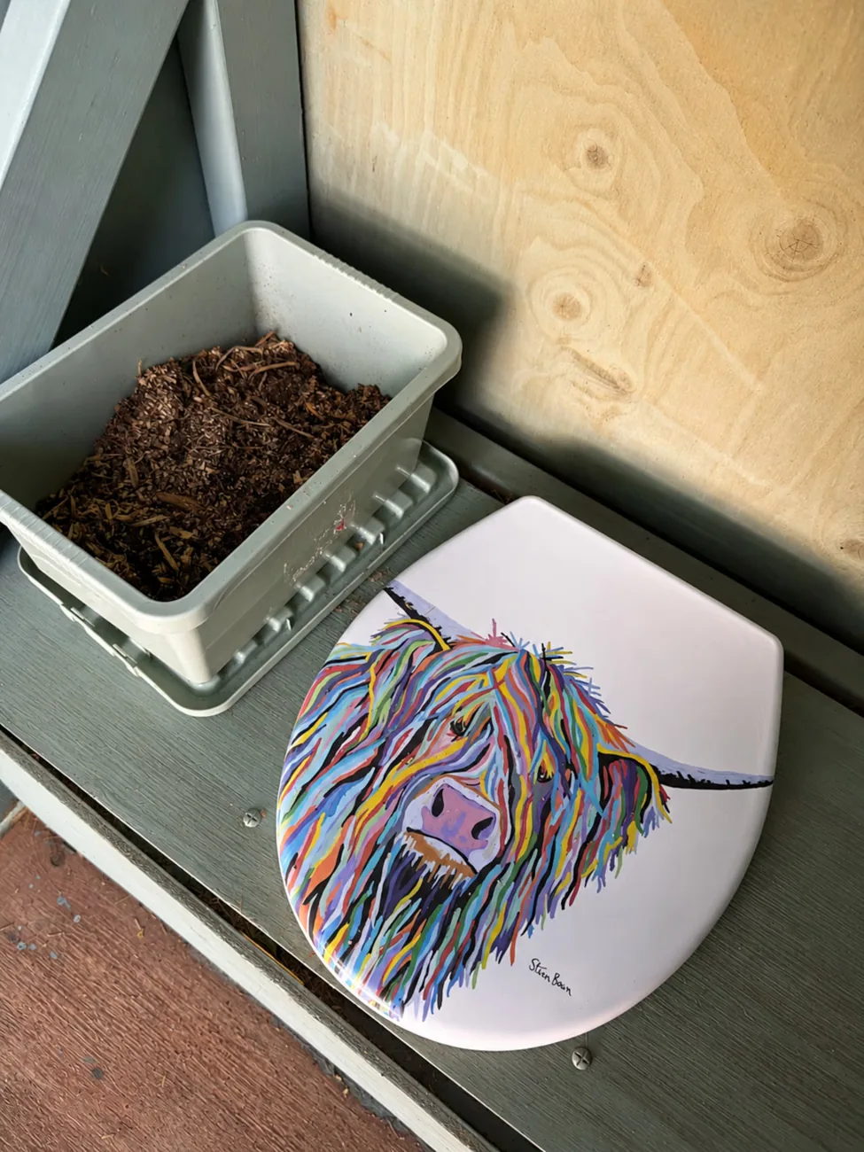 The compost loo with its hand-painted Highland cow lid and kindling beside it