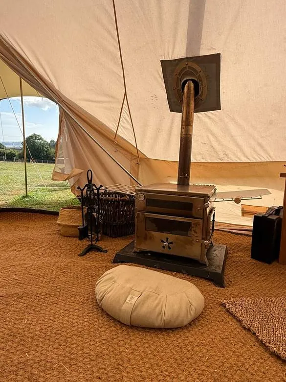 A wood burner and meditation cushion inside the tent, with the field beyond the door